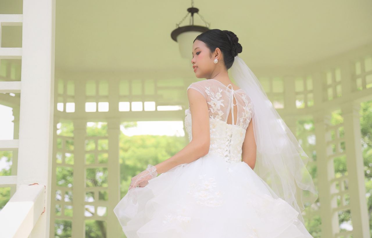 Bride in a white gown viewed from behind in an outdoor pavilion