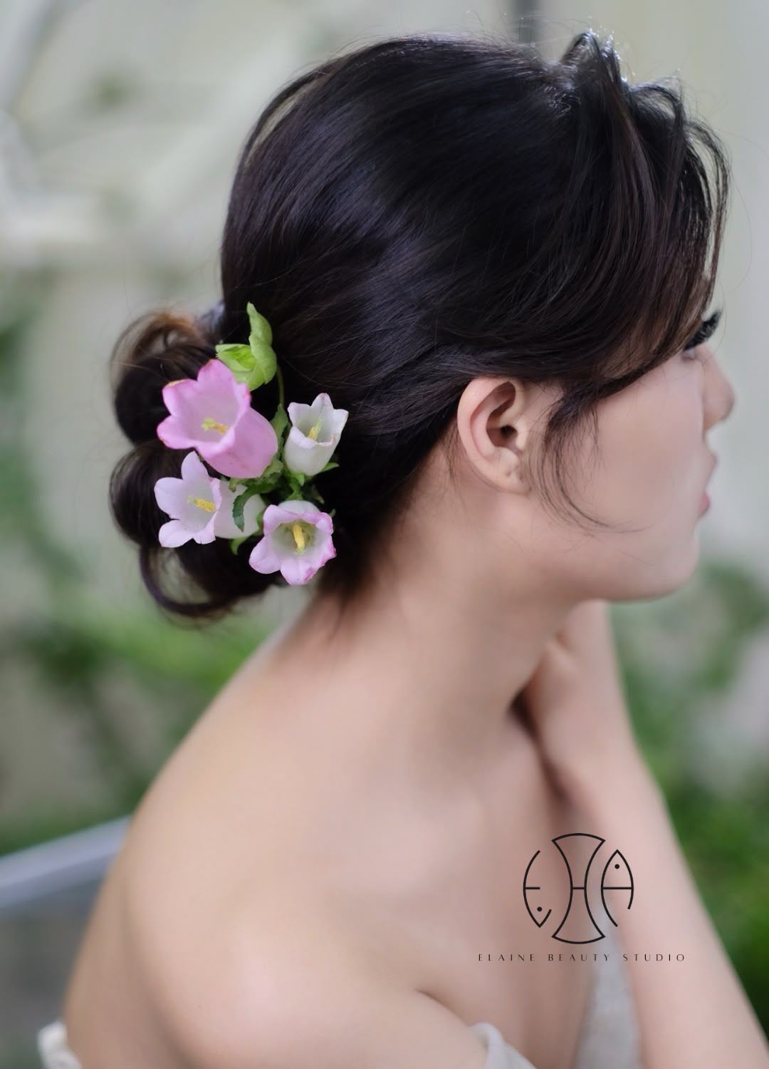 Low bridal bun with pink and white floral accents by Elaine Beauty Studio