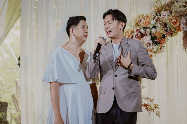 Emcee JonTee speaking into a microphone beside a wedding couple
