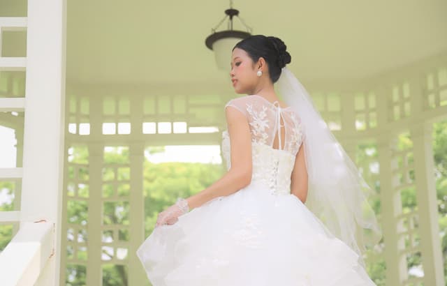 Bride in a white gown viewed from behind in an outdoor pavilion